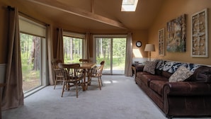 A spacious living room with a large window, a dining table with chairs, a brown leather sofa, and a lamp.