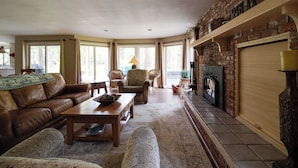 A cozy living room with a leather sofa, patterned armchairs, a wooden coffee table, and a fireplace.