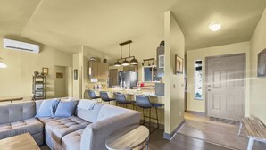 Een moderne woonkamer met een hoekbank, een eethoek met barkrukken, een keuken met roestvrijstalen apparatuur en een houten vloer.