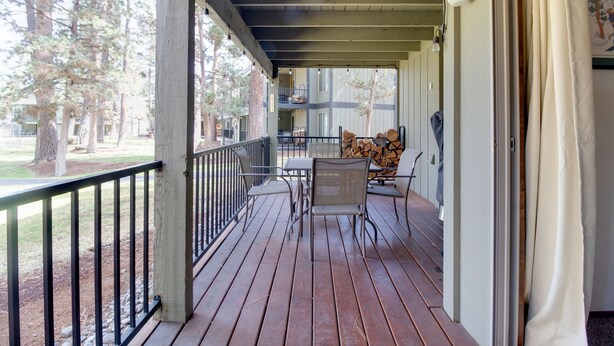 A wooden deck with a table and chairs, a railing, and a view of trees and buildings in the background. - Fourth Sister Getaway Condo 2 bdrm 2 bth sleeps 6, fireplace, community pool/spa (Sisters)
