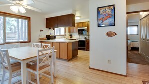 A modern kitchen with wooden cabinets, a central island, and a dining area with white chairs. - Fourth Sister Getaway Condo 2 bdrm 2 bth sleeps 6, fireplace, community pool/spa (Sisters)