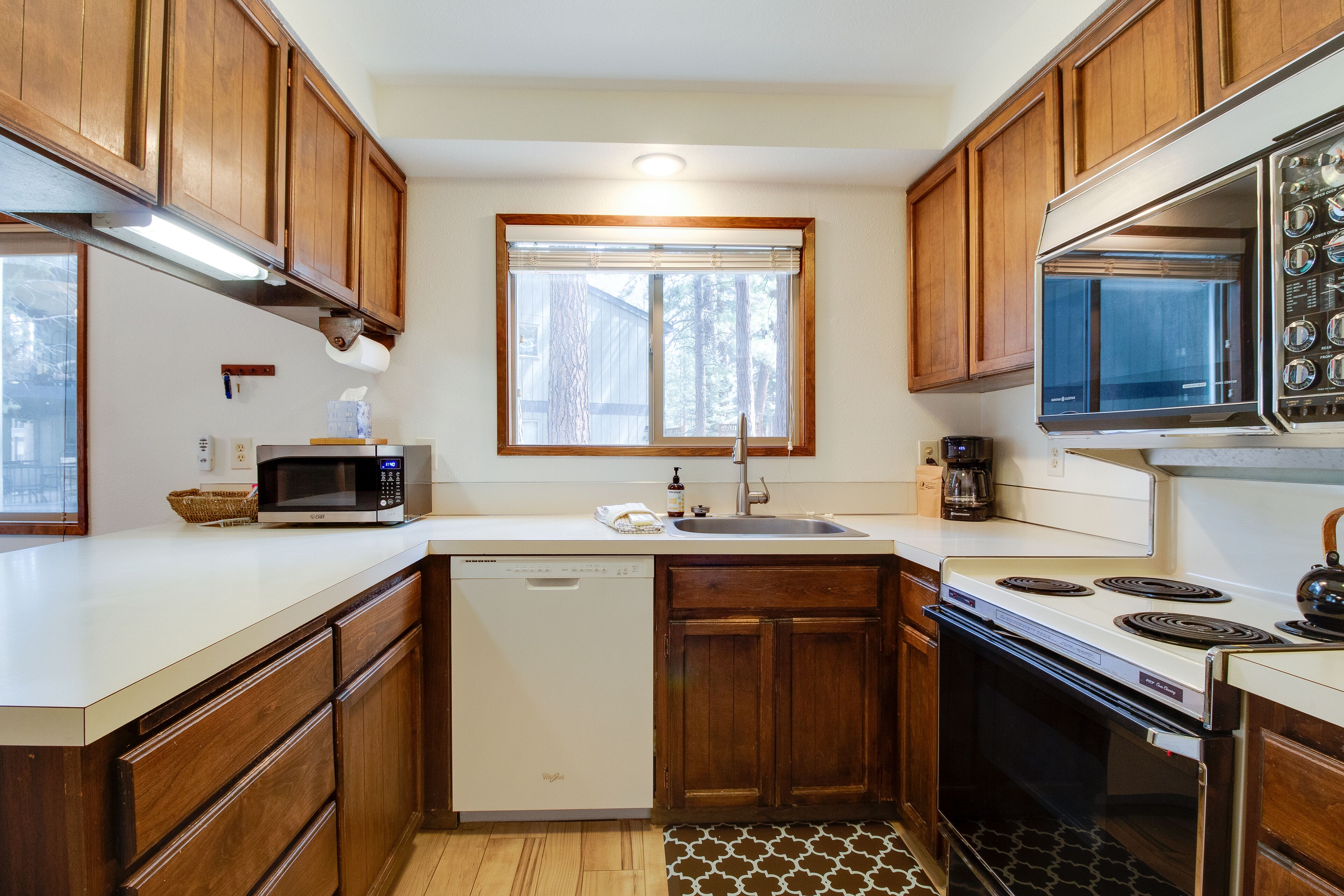 A kitchen with wooden cabinets, a microwave, a dishwasher, a stove, and a window with blinds.