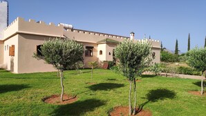 A building with a beige facade, a turret, and a small garden with young trees. - Maison Avec Piscine Privée, Jardin Arboré, Parking Clos à 2 kms D'amizmiz (Amizmiz)