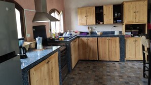 A kitchen with wooden cabinets, a granite countertop, a built-in oven, and a window. - Maison Avec Piscine Privée, Jardin Arboré, Parking Clos à 2 kms D'amizmiz (Amizmiz)
