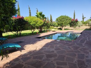 A stone-paved outdoor area with a swimming pool, surrounded by lush greenery and trees. - Maison Avec Piscine Privée, Jardin Arboré, Parking Clos à 2 kms D'amizmiz (Amizmiz)