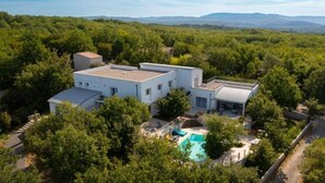 Une maison moderne à deux étages dotée d’une piscine, le tout entouré d’une végétation luxuriante.