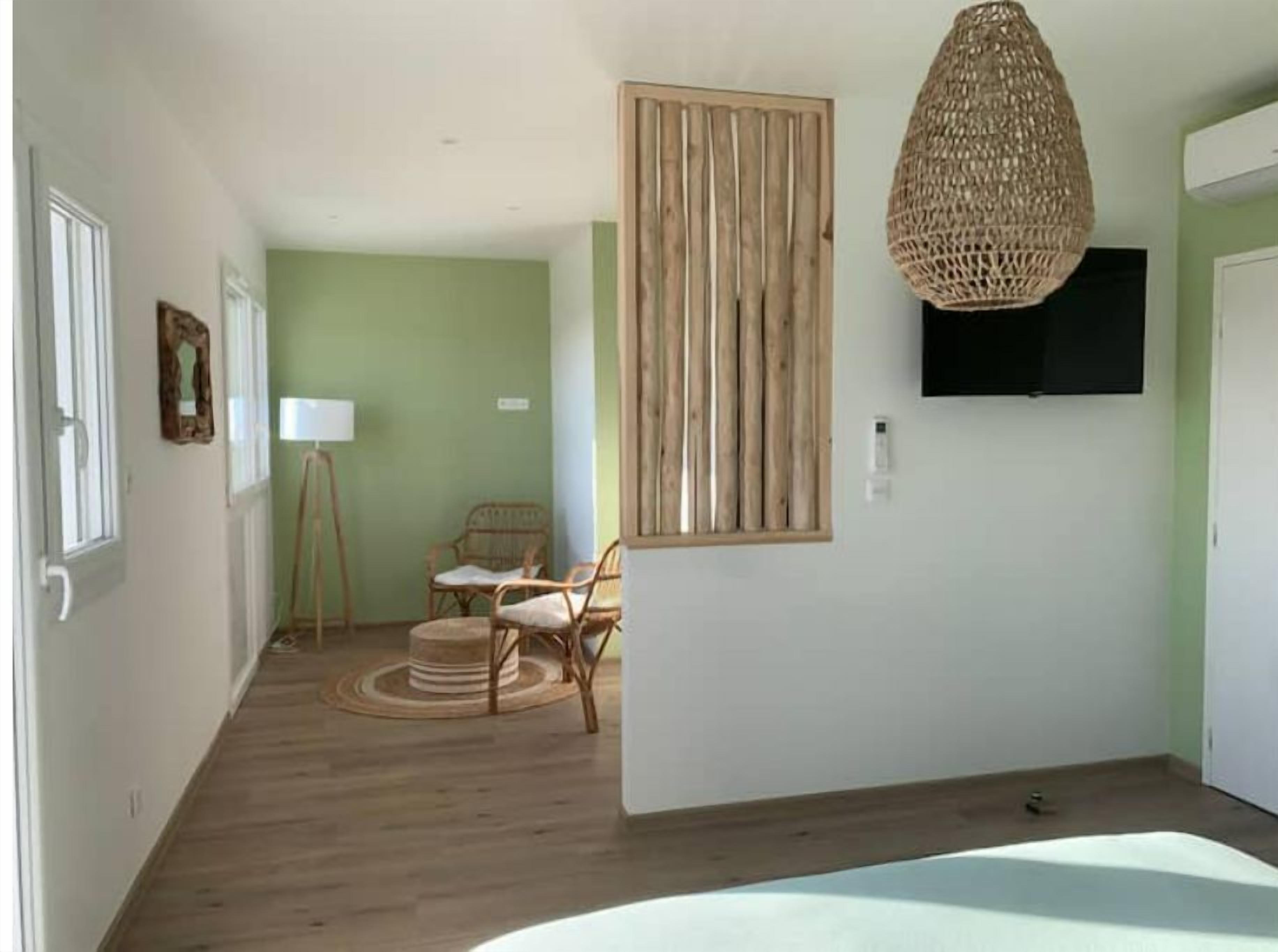 A room with a wooden floor, a wicker hanging light fixture, a television mounted on the wall, and a chair with a woven seat.