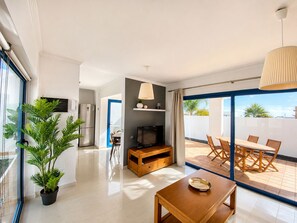 A modern living room with a TV, wooden furniture, a dining area, and a large sliding glass door leading to an outdoor patio.