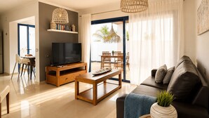 A modern living room with a TV, wooden furniture, a dining area, and a view of the outdoors. - Villa Ancor (Playa Blanca)