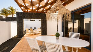 An outdoor patio with a white table and chairs, a hanging light fixture, and a stone wall. - Villa Ancor (Playa Blanca)