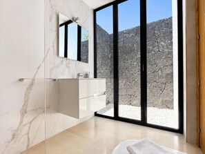 A modern bathroom with a marble wall, a glass vanity, and a large window with a view of a rocky landscape.
