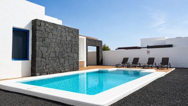 A swimming pool with lounge chairs, a stone wall, and a blue-framed window. - Villa Ancor (Playa Blanca)