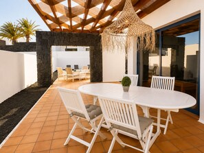 Eine Terrasse mit weißem Tisch und Stühlen, einer hängenden Leuchte und einer Steinmauer.