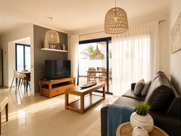 A modern living room with a TV, wooden furniture, a sofa, and a dining area with chairs and a table.