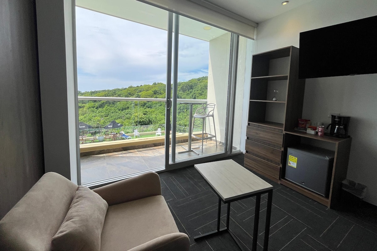 A modern room with a sofa, a small table, and a balcony with a view of greenery.