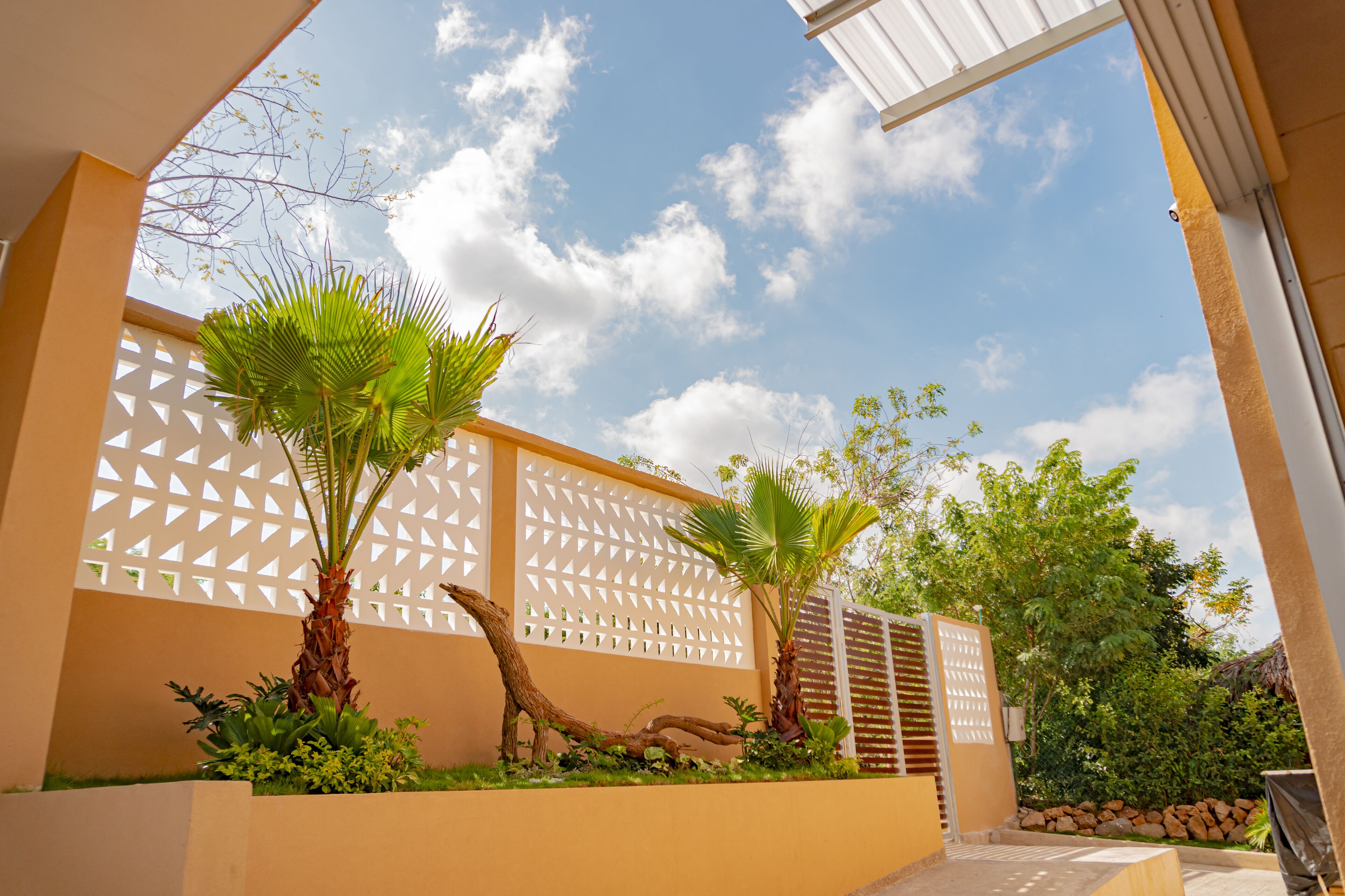 A modern outdoor area with a white lattice fence, palm trees, and a clear sky.
