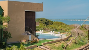 A modern building with a pool, lounge chairs, and a view of the sea.
