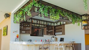 A modern kitchen with a bar area, featuring a large island with bar stools, a TV mounted above the bar, and shelves stocked with bottles and glasses.