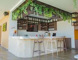 Una cocina moderna con barra, que cuenta con una isla grande con taburetes, un televisor montado sobre la barra y estantes llenos de botellas y vasos.