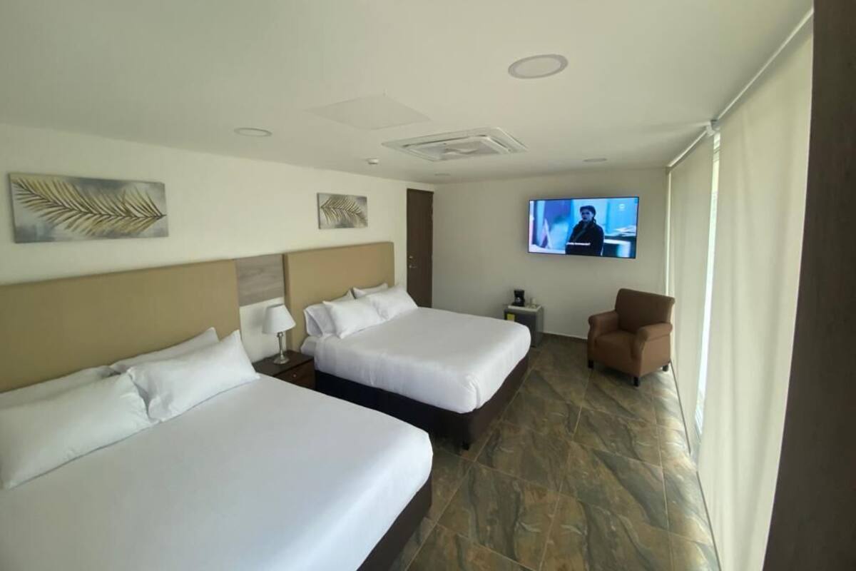 A hotel room with two beds, a TV on the wall, and a chair.