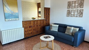 Un salon avec un canapé bleu, une petite table ronde, un radiateur, des meubles en bois et une affiche accrochée au mur.
