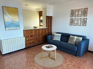 A living room with a blue sofa, a small round table, a radiator, wooden cabinets, and a poster on the wall.