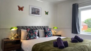 A bedroom with a tufted headboard, floral pillows, a green bedspread, and two bedside lamps.