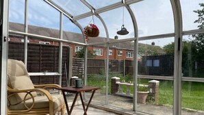 A conservatory with a wicker chair, a small table, and hanging plants.