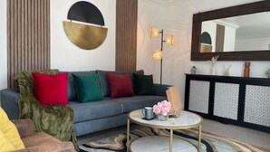 A modern living room with a grey sofa, colorful cushions, a round coffee table, and a patterned rug.