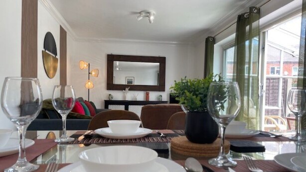A dining area with a table set for two, a sofa, a mirror, and a window with a view of buildings.