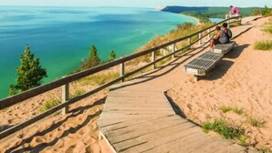 Ein hölzerner Steg führt zu einem Sandstrand mit Blick auf das Meer und das entfernte Land.