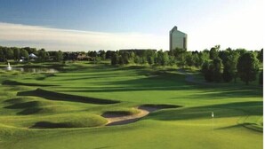 Ein Golfplatz mit Bunkern, einer Fahne und einem Gebäude im Hintergrund.