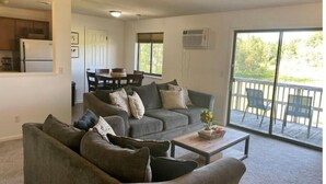 Ein Wohnzimmer mit grauem Sofagarnitur, einem Couchtisch und einer Glasschiebetür, die auf einen Balkon führt.