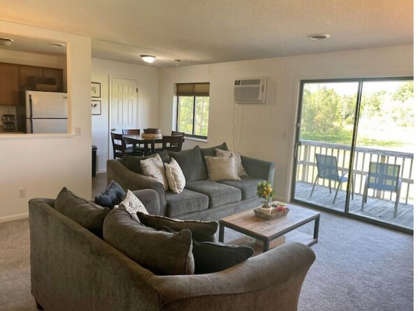 A living room with a grey sofa set, a coffee table, and a sliding glass door leading to a balcony.