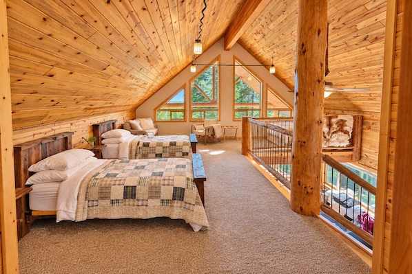 A bedroom with two beds, a wooden ceiling, and large windows.