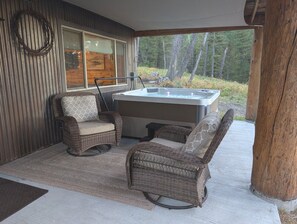 A covered outdoor area with wicker furniture, a hot tub, and a view of a forest.