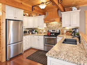 A kitchen with white cabinets, a stainless steel refrigerator, a stove, and a granite countertop. - Ranked top 1% of Yellowstone and Grand Teton region cabins to stay at (Island Park)