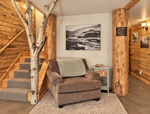 A cozy room with a brown sofa, a wooden staircase, and a large wall-mounted picture. - Ranked top 1% of Yellowstone and Grand Teton region cabins to stay at (Island Park)
