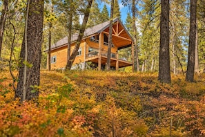A wooden cabin with a balcony, surrounded by a forest with autumn foliage. - Ranked top 1% of Yellowstone and Grand Teton region cabins to stay at (Island Park)