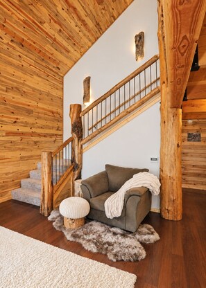 Una escalera de madera con diseño rústico, un sofá gris y una alfombra mullida en una habitación con paredes y suelos de madera.