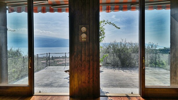 Quarto com uma grande porta de vidro deslizante que dá para um deck ao ar livre com vista para o mar e montanhas.