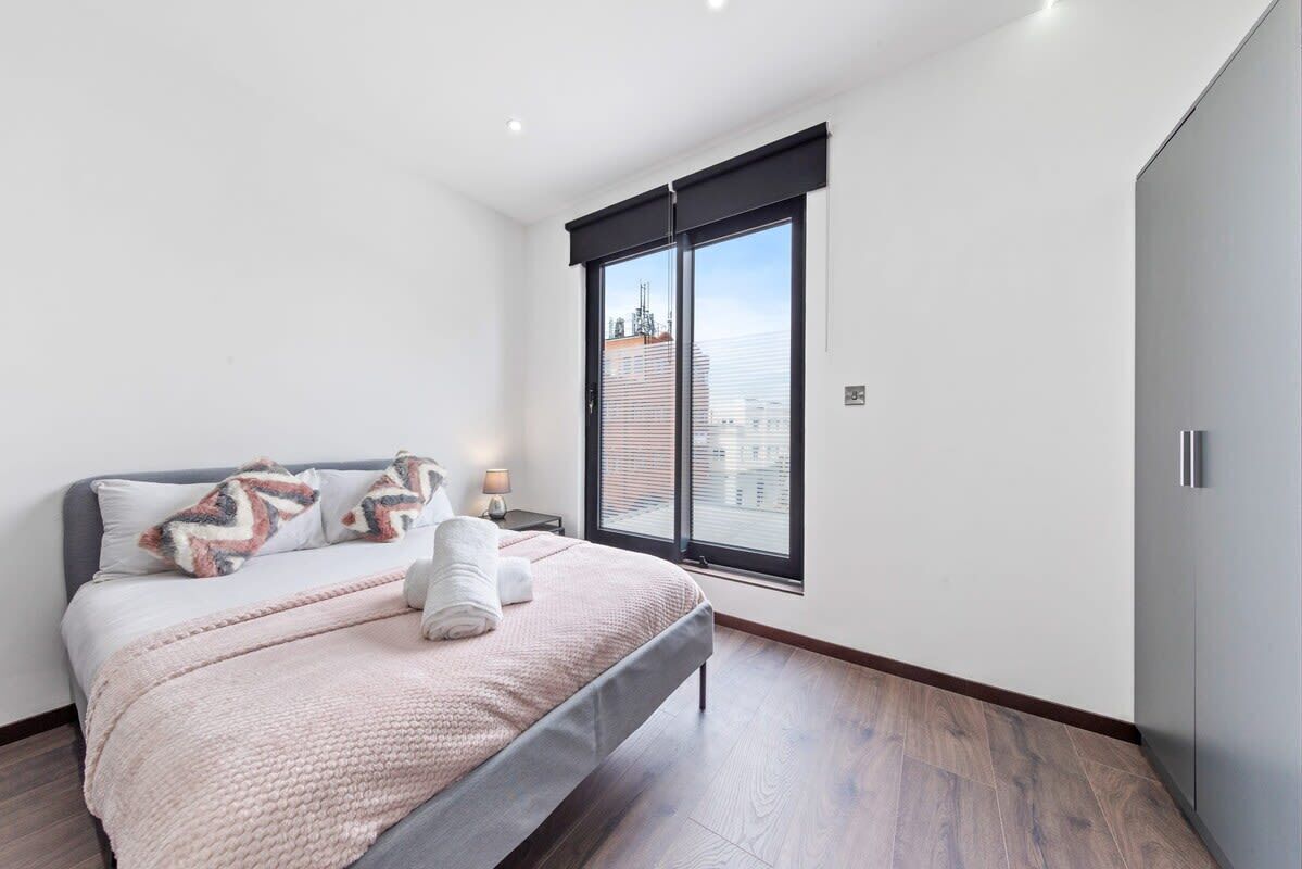 Un dormitorio moderno con una cama grande, una ventana que ofrece vistas a edificios y un armario.