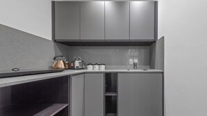A modern kitchen with grey cabinets, a stainless steel kettle, a coffee maker, and a toaster. - Serviced Studio Flat near Camden Euston Station (Greater London)