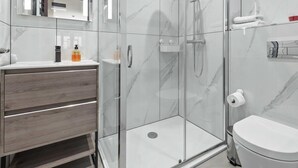 A modern bathroom with a glass-enclosed shower, a wooden vanity, and a white toilet. - Serviced Studio Flat near Camden Euston Station (Greater London)