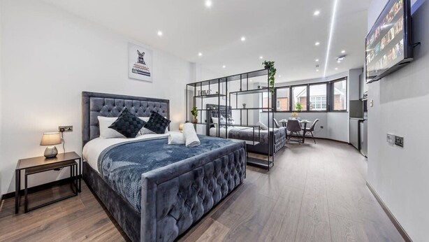A modern bedroom with a large bed, bedside tables, a TV, and a view of the city.