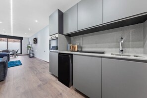 Een moderne keuken met grijze kastjes, een zwarte vaatwasser en een RVS-spoelbak.