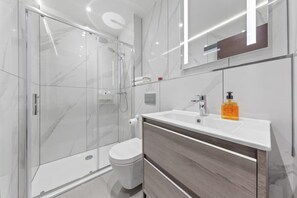 A modern bathroom with a glass shower enclosure, a white toilet, and a vanity with a mirror.
