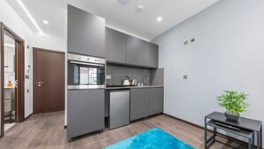 A modern kitchen with grey cabinets, a built-in oven, and a dishwasher. There is a small table with a plant and a remote control.