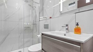 A modern bathroom with a glass shower enclosure, a white toilet, and a vanity with a marble countertop.
