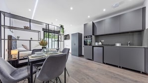 Une cuisine moderne avec des meubles de couleur grise, un coin repas avec une table et des chaises, et une fenêtre donnant sur un espace extérieur verdoyant.